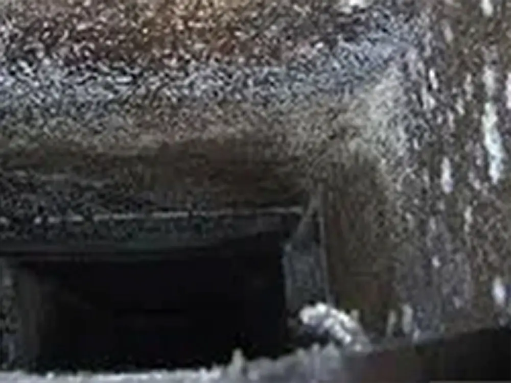 Close-up view of a dark and sooty chimney interior, reminiscent of neglected air ducts. The walls are covered in a thick layer of black soot, with lighter ash deposits peeking through. Extending into darkness at the bottom, it suggests depth and a gritty texture that would benefit from professional cleaners near me.